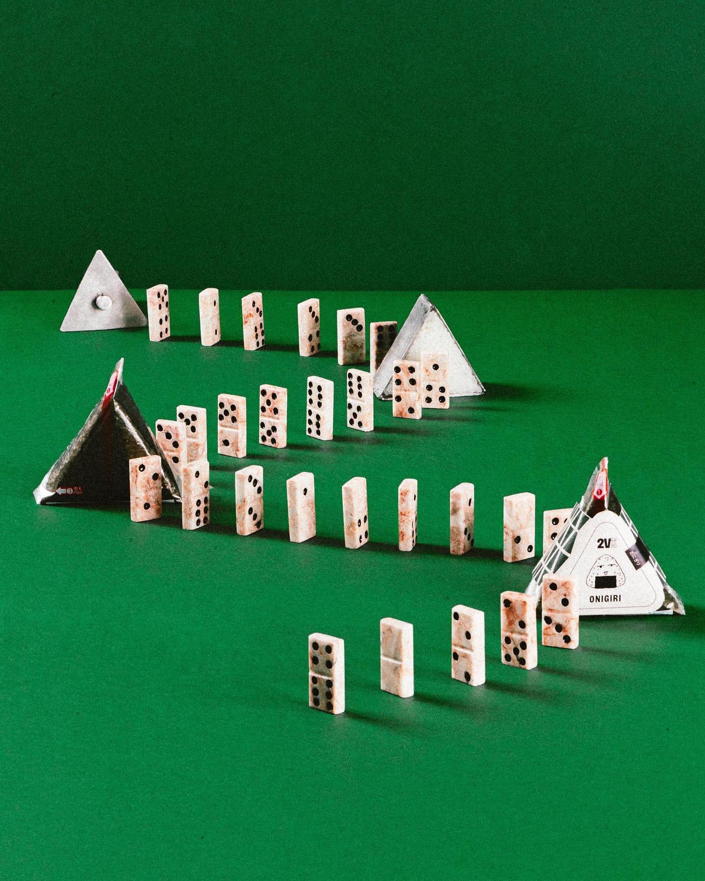 Still: onigiris embalados no meio de uma fileira de peças de dominó sobre fundo verde