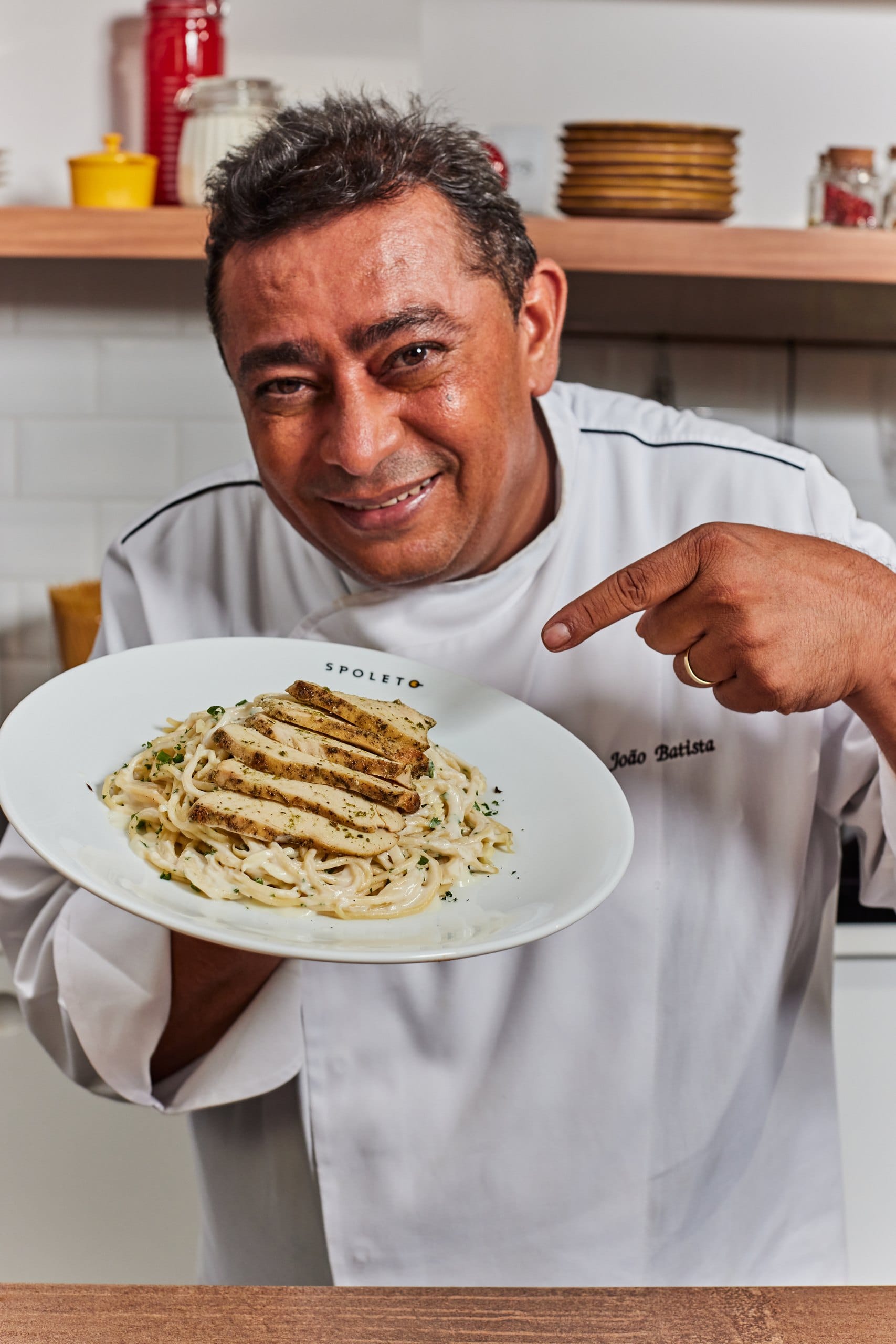 O chef João Batista aponta para um prato de massa com frango grelhado