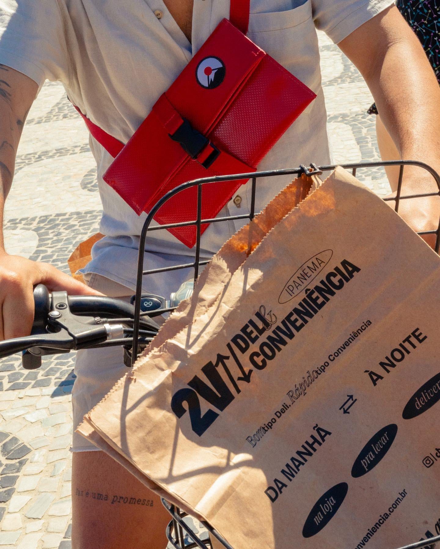 Ciclista no calçadão de Ipanema com a sacola de papel da 2V Deli & Conveniência na cestinha