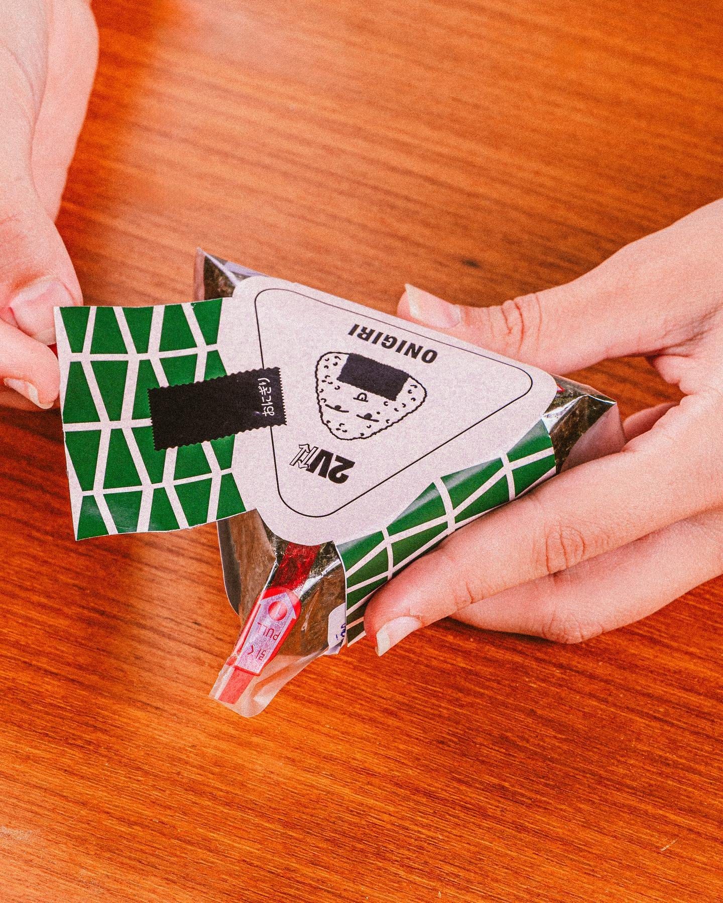 Mãos abrindo a embalagem triangular do onigiri da 2V