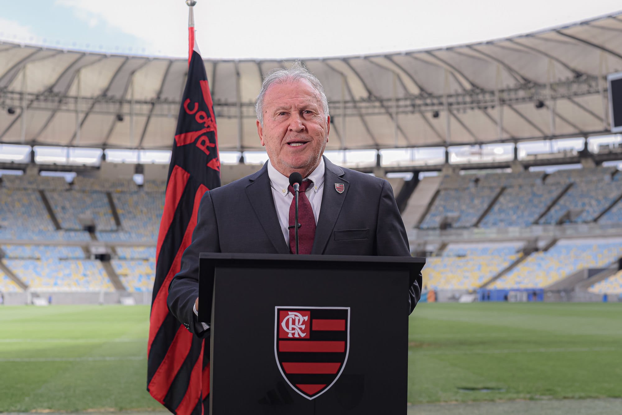 Zico discursa no púlpito com o escudo do Flamengo, ao lado da bandeira rubro-negra