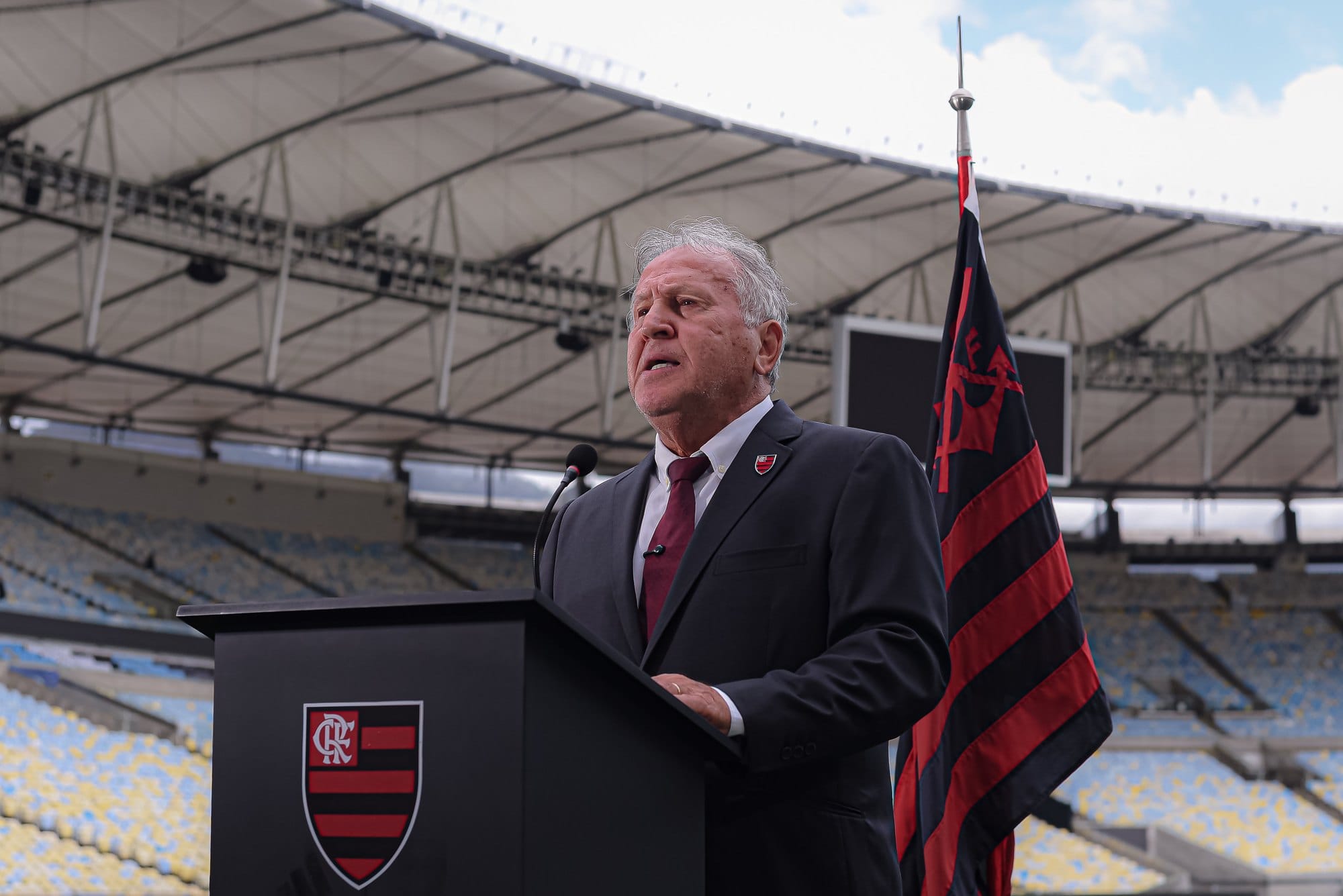 Zico discursa diante da bandeira do Flamengo, com o telão do estádio ao fundo