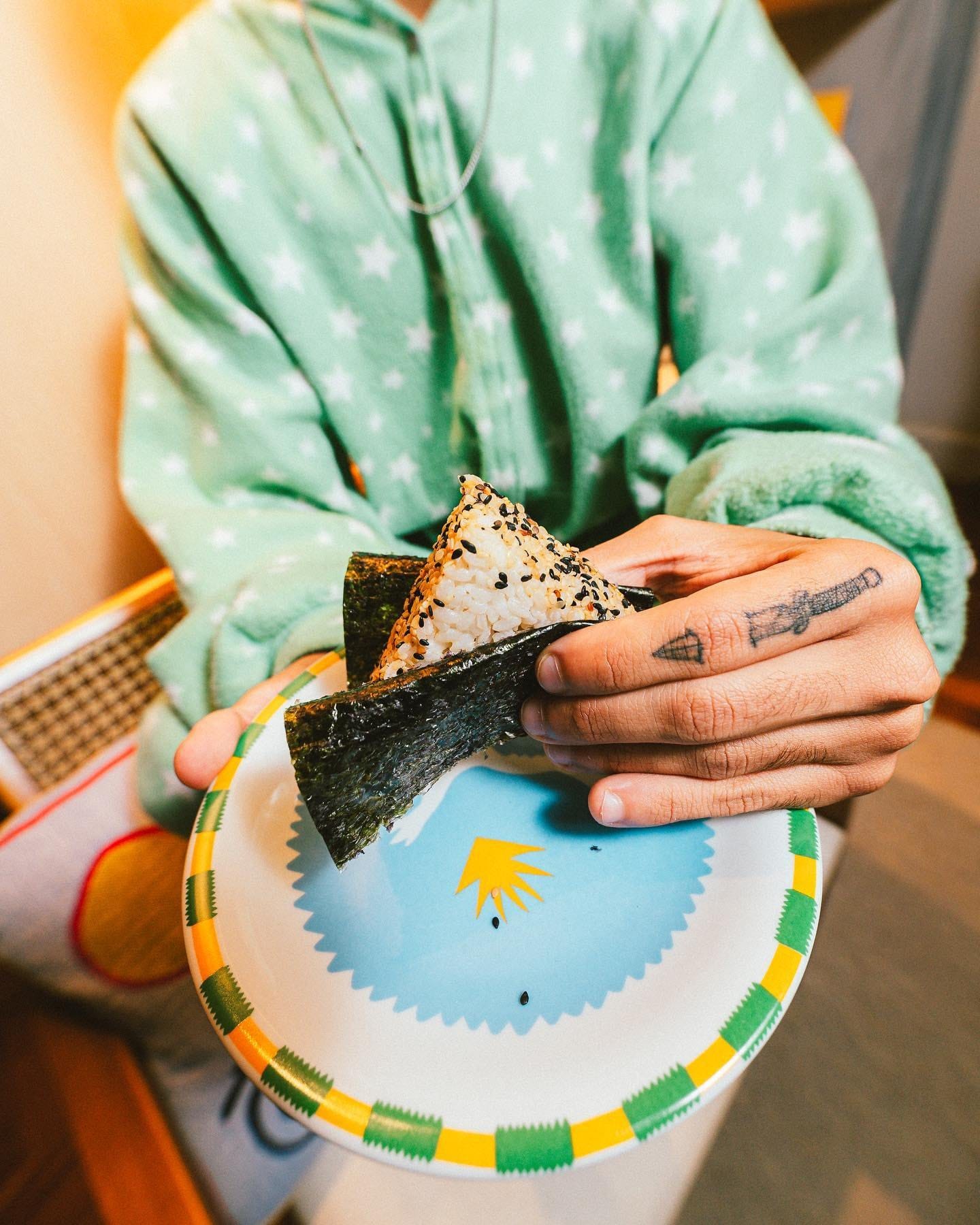 Onigiri envolto na alga crocante, nas mãos, sobre um prato colorido